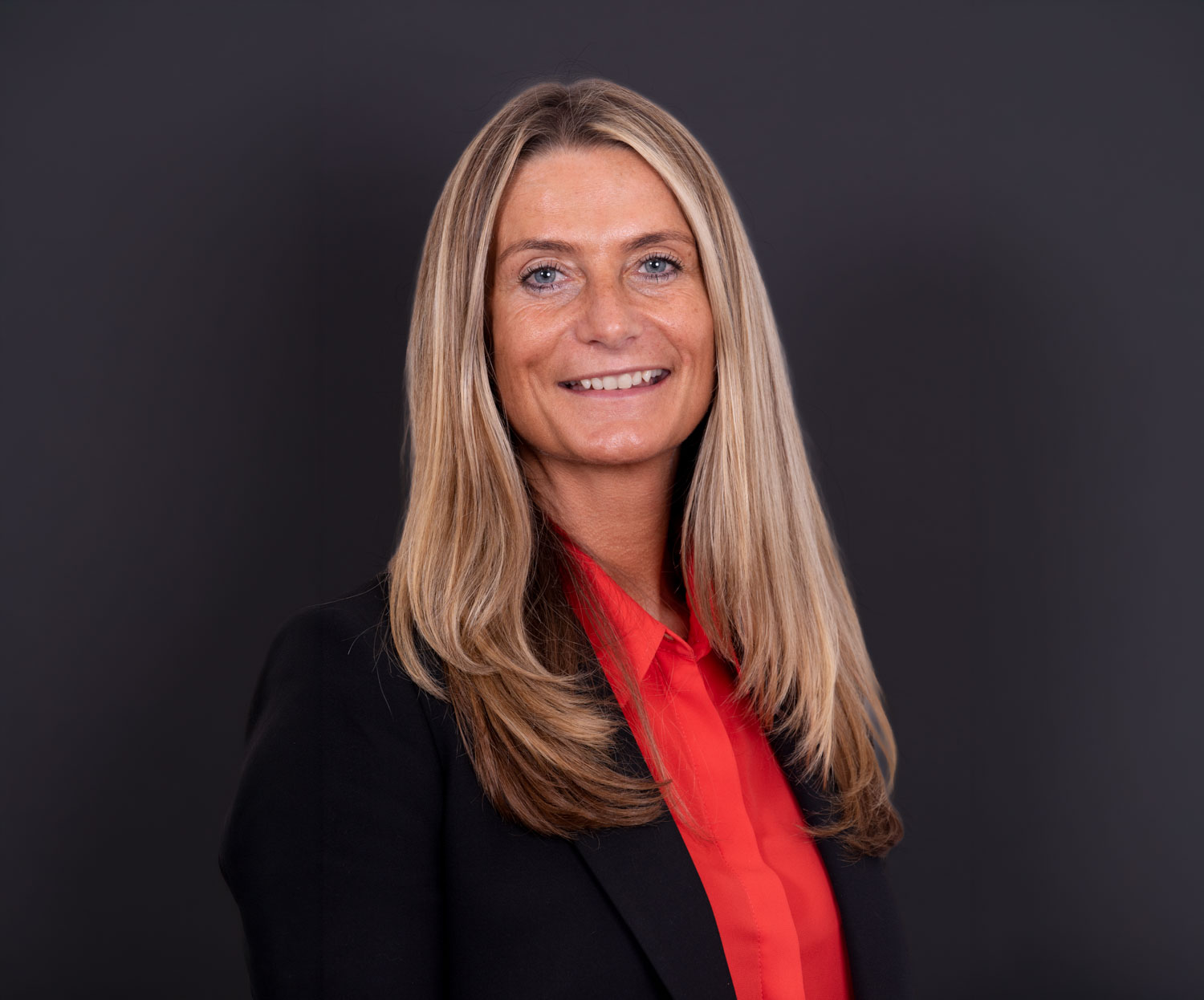 Executive headshot of a businesswoman in a black blazer on a dark studio backdrop