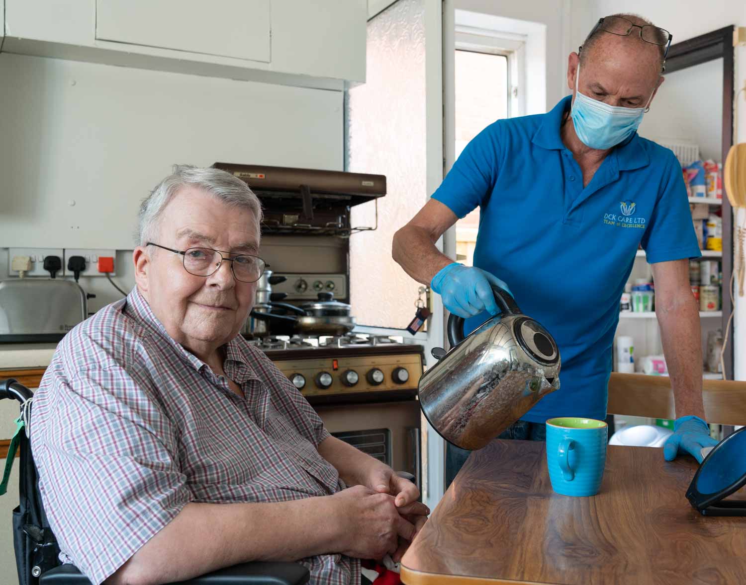 Home care worker making a cup of tea for an older client in his kitchen