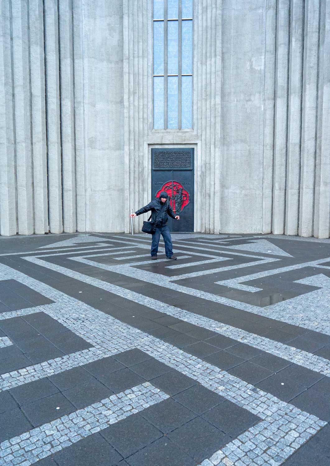 Lone figure walking across the patterned plaza in front of a concrete cathedral facade